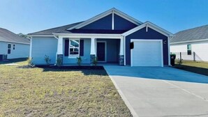 Une maison de plain-pied à l’extérieur bleu foncé, avec un garage à l’avant et un petit jardin devant la maison, composé de pelouse et d’une allée en béton.