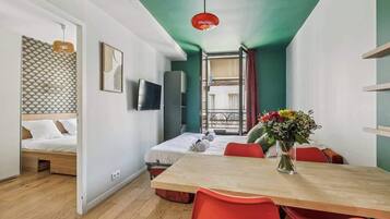 Una habitación con cama, una mesa de comedor con sillas, un televisor y un ventanal con cortinas.