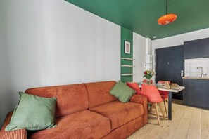 Uma sala de estar com sofá, uma mesa de jantar com cadeiras, uma área de cozinha e uma parede verde.