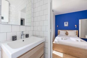 Habitación de hotel con un lavamanos blanco, tocador de madera, cama con ropa blanca y una pared de acento azul.