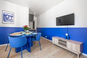 Un comedor con una mesa dispuesta para dos personas, sillas azules, un armario de madera y un televisor de pantalla plana montado en la pared.