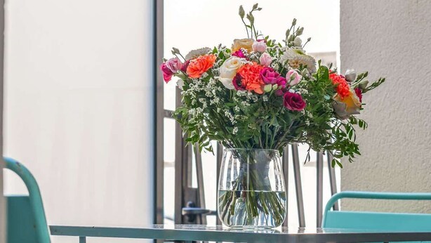 A glass table with a vase of flowers, two teal chairs, and a metal railing.