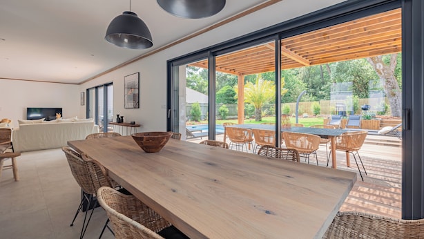 A modern kitchen with a large wooden table, wicker chairs, and a TV.