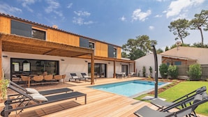 A modern house with a wooden deck, a swimming pool, and outdoor seating.