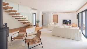 A modern living room with a staircase, a sofa set, a TV, and a fireplace.