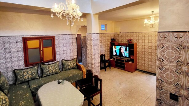 A spacious living room with a high ceiling, a chandelier, a television, and patterned walls.