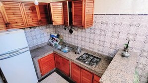 A compact kitchen with wooden cabinets, a gas stove, a sink, and a refrigerator.