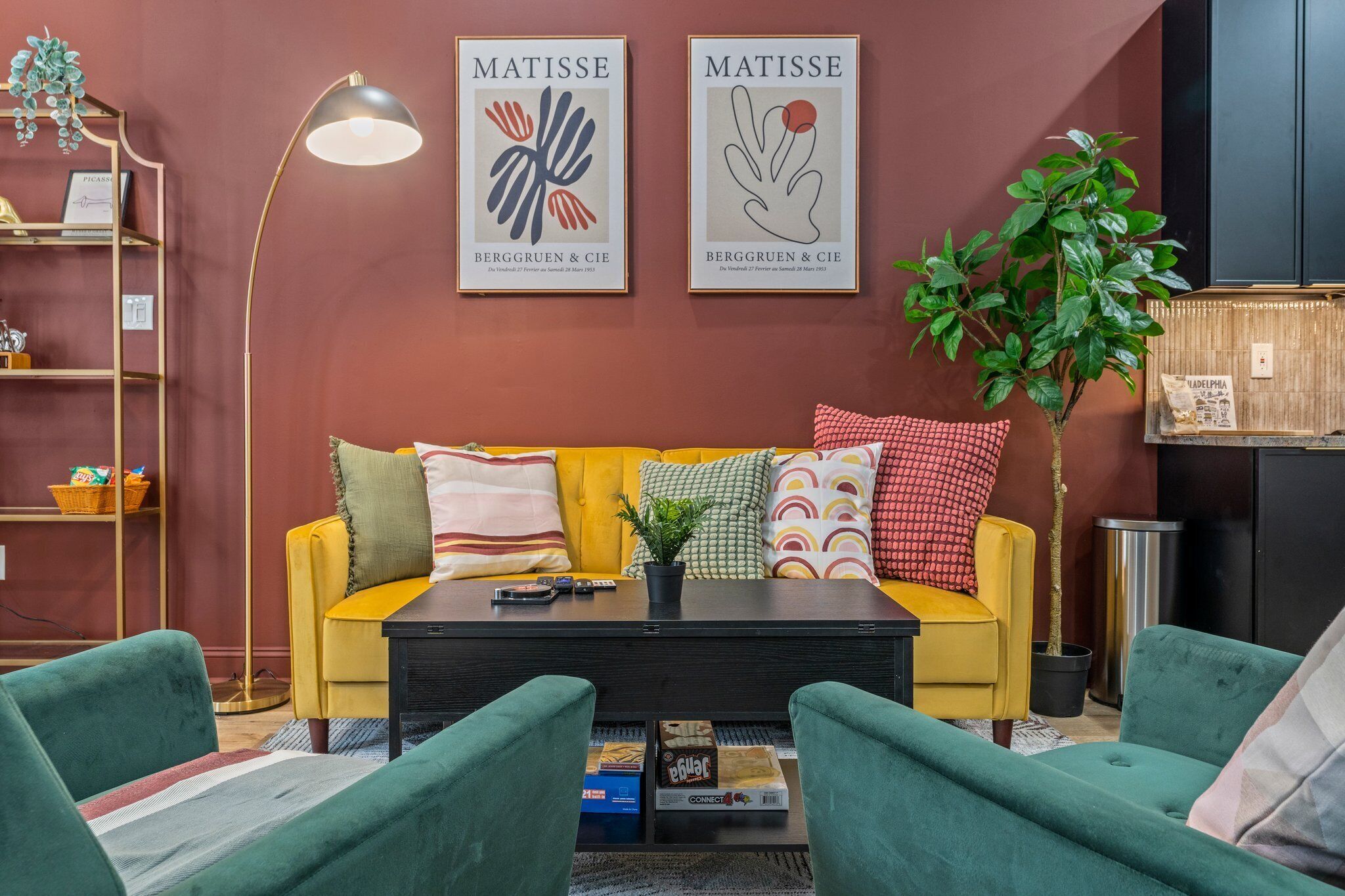 A living room with a yellow sofa, green armchairs, a coffee table, and two framed artworks on the wall.
