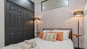 A neatly made bed with rolled towels, a patterned wall, and two floor lamps. - Old City History Kid-Friendly (Philadelphia)