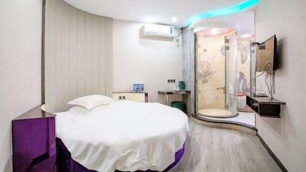 A modern hotel room with a curved bed, a shower enclosure, a mounted TV, and a small desk with a chair. - Yixin Hotel (Shanghai Guilin Road Subway Station) (Shanghai)