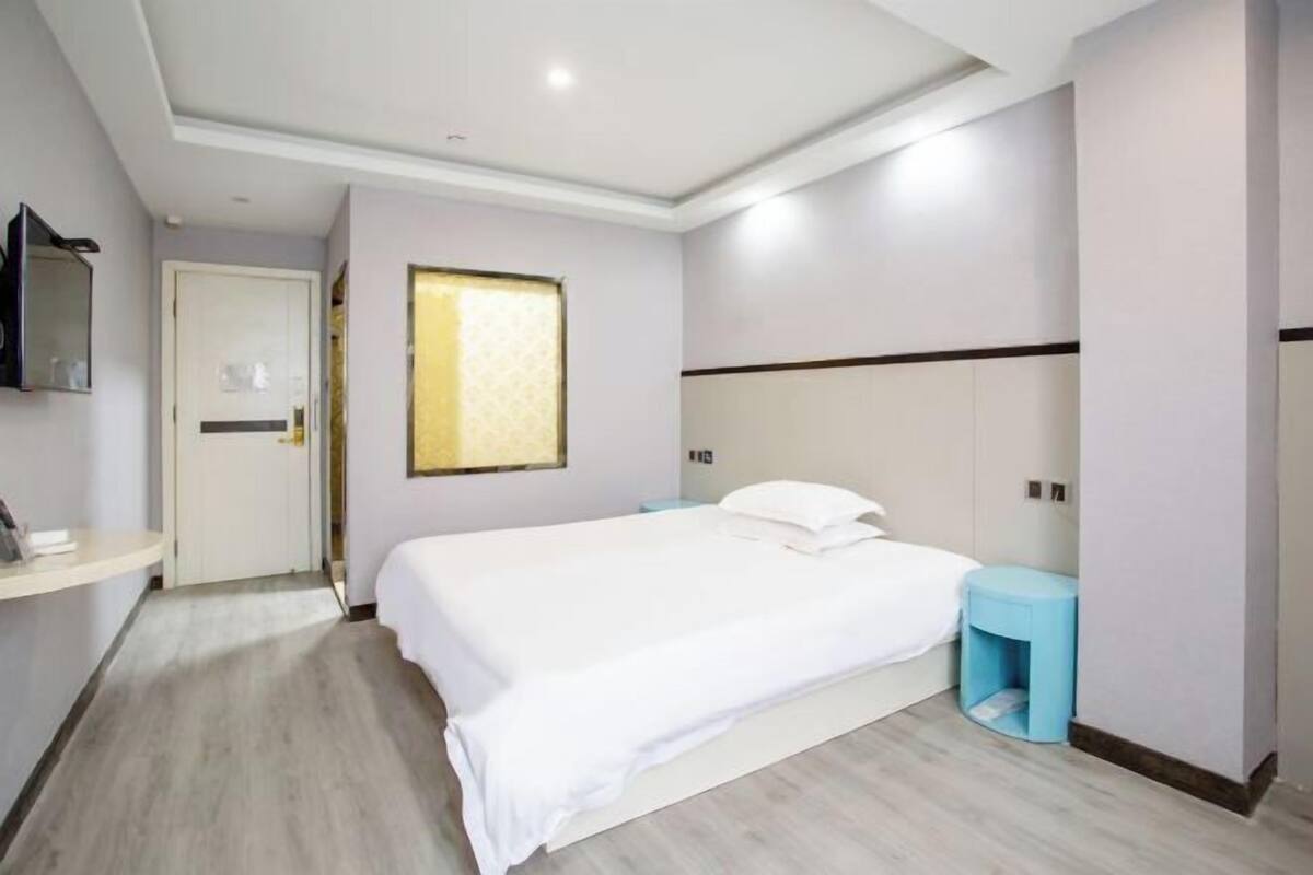A hotel room with a bed, bedside tables, a mirror, and a window.
