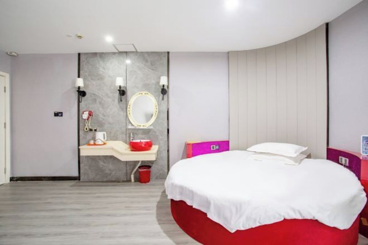 Un dormitorio moderno con una cama curvada, un tocador con espejo y una pared de acento roja.