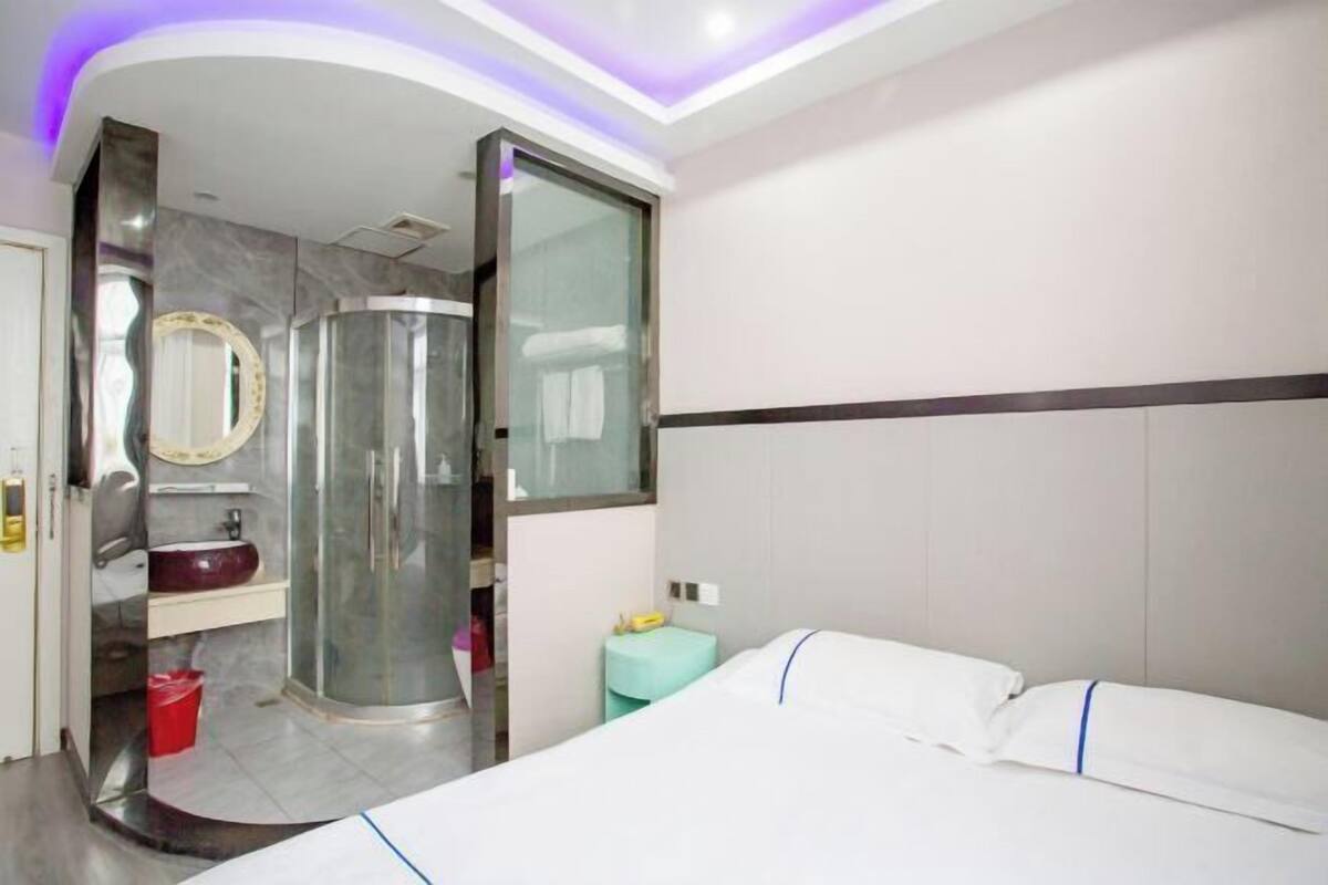 A hotel room with a bed, a bathroom with a shower, a mirror, and a small table.