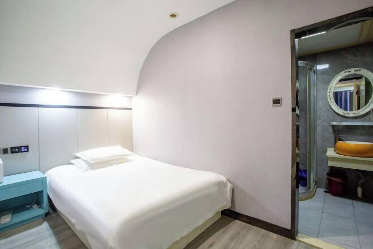 A hotel room with a bed, a nightstand, a bathroom with a mirror and sink.