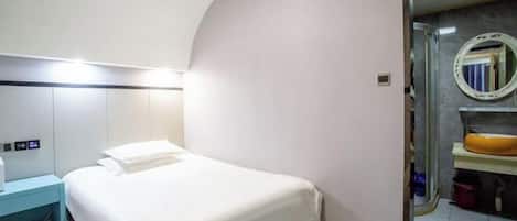 Habitación de hotel con cama, mesita de noche y baño con espejo y lavamanos.