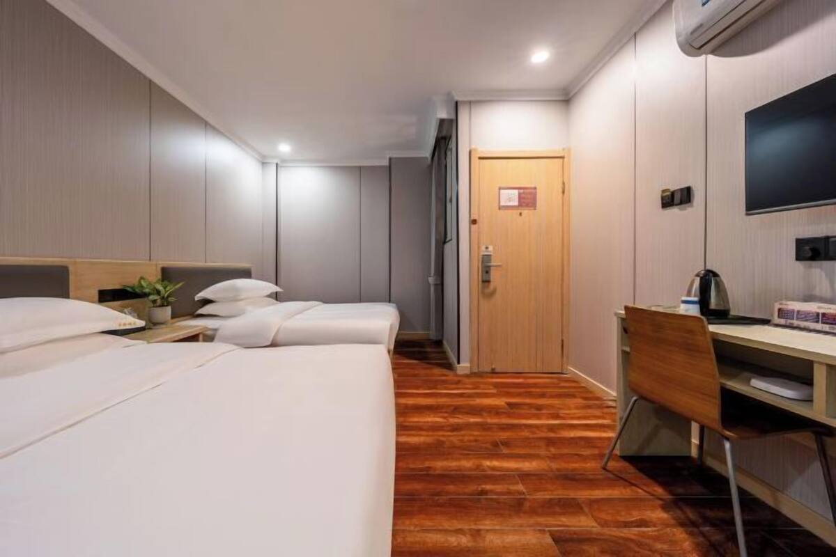Une chambre d’hôtel avec deux lits, un bureau, une chaise, une télévision et un plancher en bois.