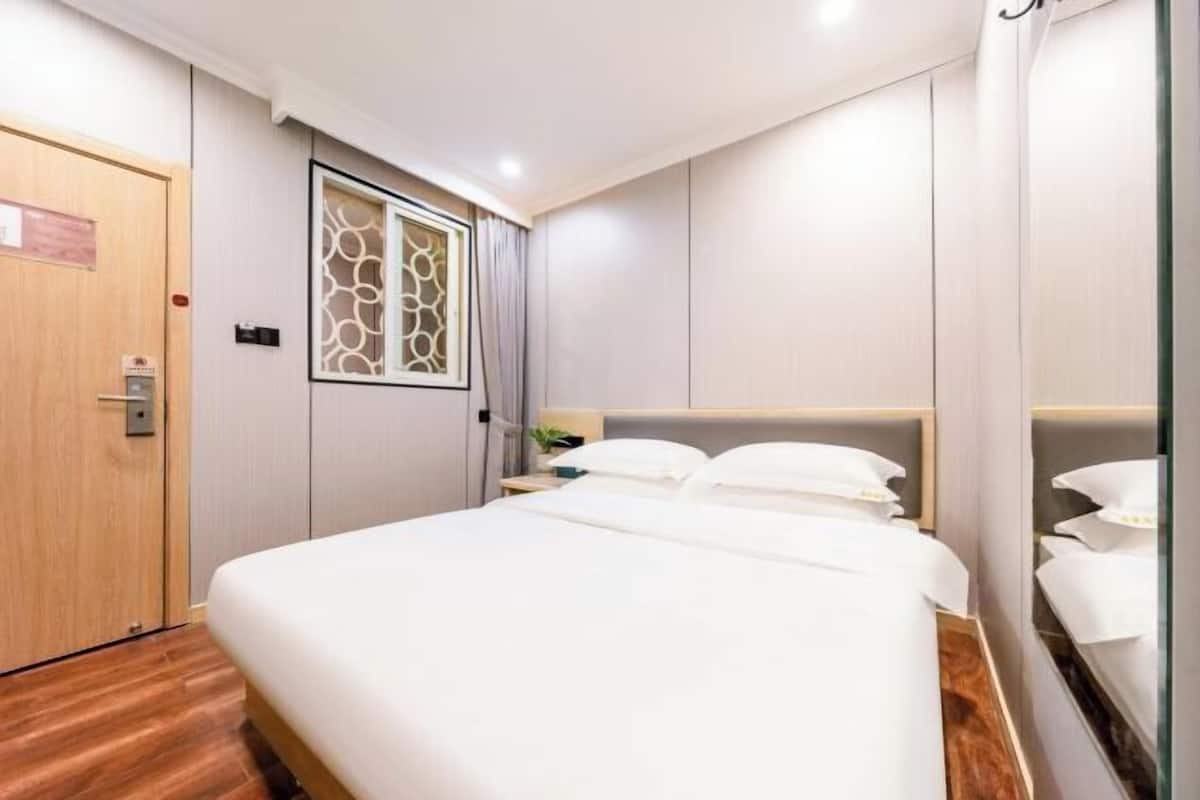 Une chambre d’hôtel avec un grand lit, une porte en bois, une fenêtre ornée d’un paravent décoratif et un miroir au mur.