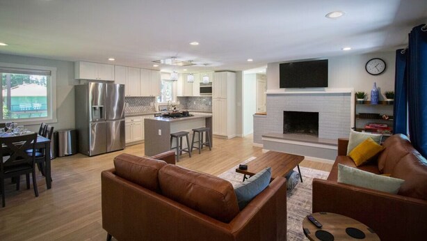 A modern kitchen with stainless steel appliances, a dining area with a table and chairs, and a living room with a brown leather sofa and a fireplace.