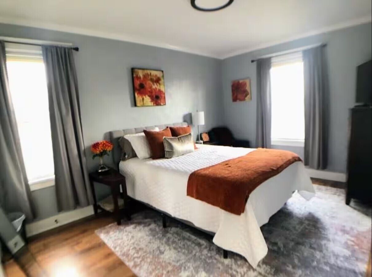 Une chambre à coucher avec un grand lit, une table de chevet, une commode et une fenêtre avec des rideaux.