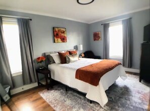 A bedroom with a large bed, a nightstand, a dresser, and a window with curtains. - Comfortable and Convenient! (Mountlake Terrace)