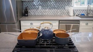 A kitchen with a gas stove, three pots, and a kettle.