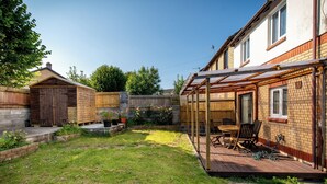 A backyard with a wooden deck, a brick house, and a wooden shed.