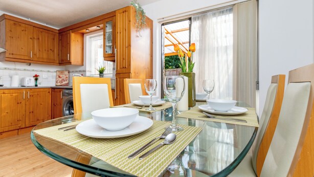 A modern kitchen with wooden cabinets, a glass dining table, and a view of the outdoors through a large window.