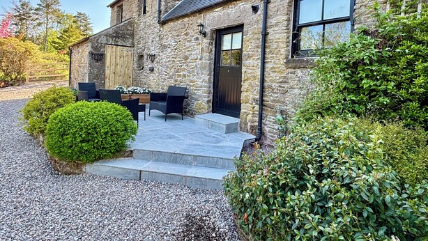 A stone building with a black door, a patio with outdoor furniture, and a gravel driveway.