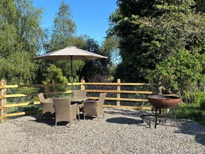 Une terrasse extérieure aménagée avec des meubles en osier, un barbecue en métal et une clôture en bois.