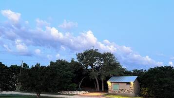 A small stone building with a metal roof, surrounded by trees and a grassy area.