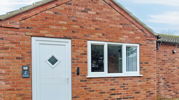 A brick house with a white door and window, a wooden deck, and a small plant in the foreground. - 1 bedroom accommodation in Walcott (Walcott)