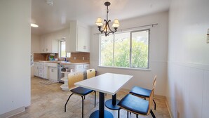 A kitchen with a dining area, a chandelier, and a window with a view of trees.