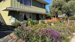 A two-story house with a front porch and a garden with various plants and flowers.