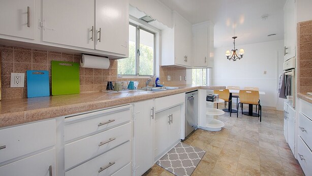 A modern kitchen with white cabinets, a built-in dishwasher, and a dining area with a table and chairs.