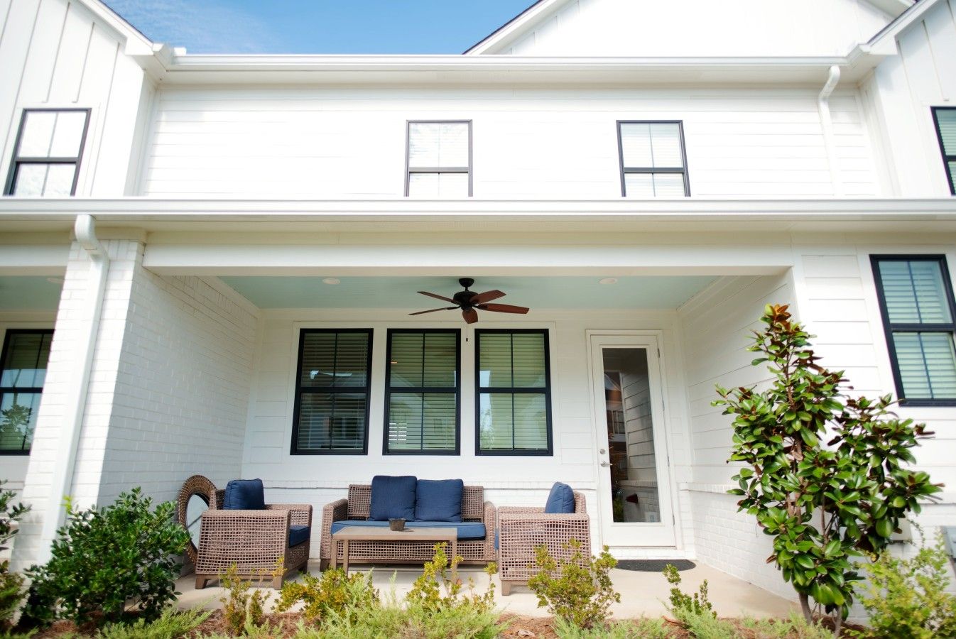A two-story house with a covered porch, a ceiling fan, and a door leading to the interior.