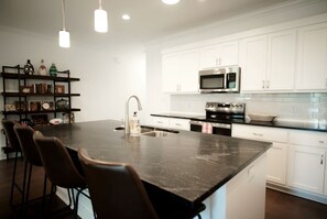 A modern kitchen with white cabinets, a stainless steel microwave, and a large island with bar stools. - Luxurious Property in the Heart of Oxford (Oxford)