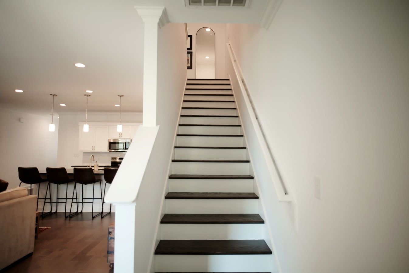 A modern staircase with a minimalist design, leading to a kitchen area with white cabinetry and stainless steel appliances.