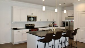 A modern kitchen with white cabinetry, stainless steel appliances, a central island with bar stools, and pendant lighting. - Luxurious Property in the Heart of Oxford (Oxford)