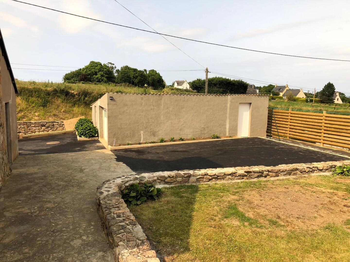 A courtyard with a paved area, a stone wall, and a wooden fence.