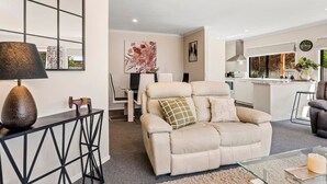 Una sala de estar moderna con un sofá color beige, una mesa de centro de vidrio y una mesita auxiliar de metal negro.