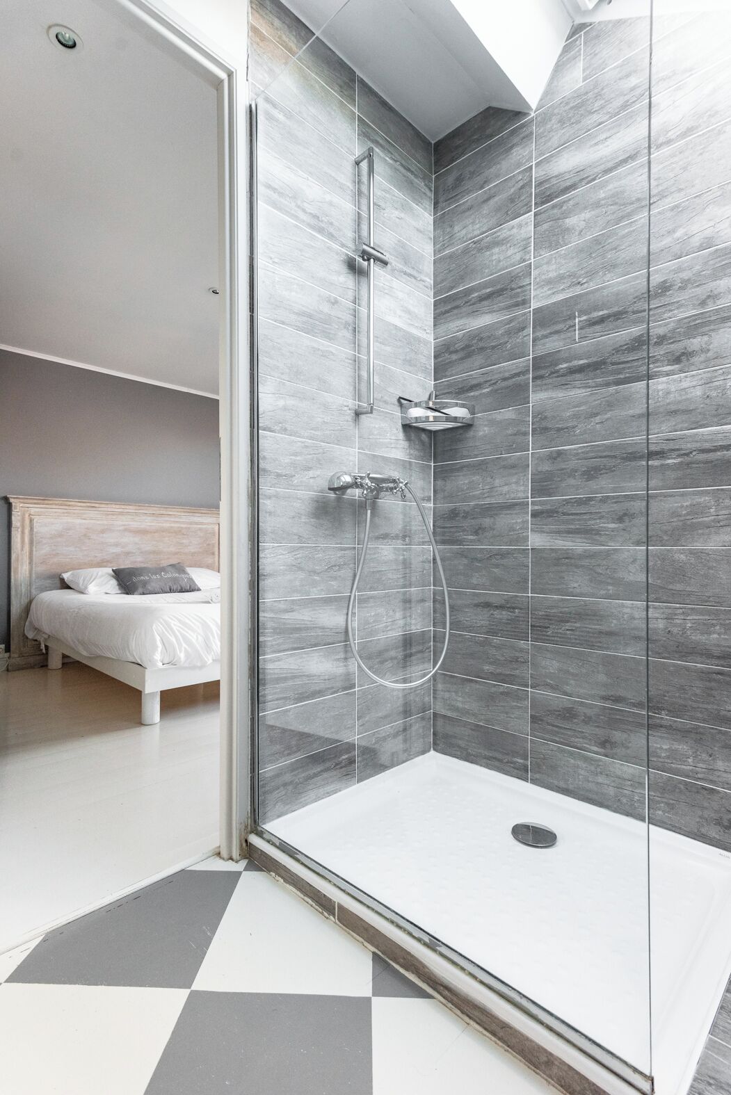 A modern bathroom with a shower, a glass-enclosed shower area, and a bed in the adjacent room.