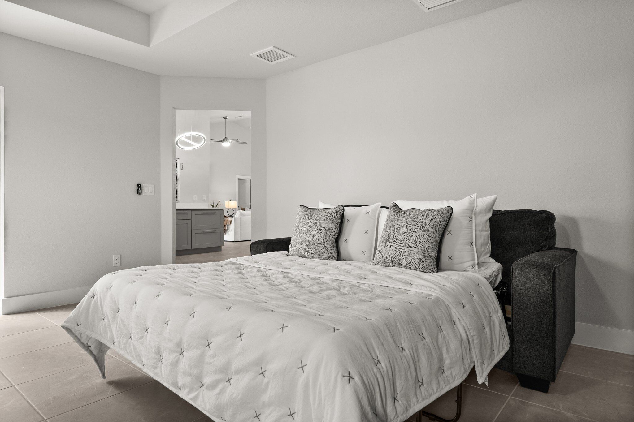 A modern bedroom with a large bed, a dark armchair, and a mirror above the bed.