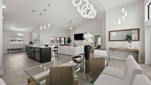 A modern kitchen with a central island, a dining area with a glass table, and a living space with a large mirror and a TV. - Paradise in front of the water (Cape Coral)