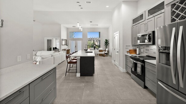 A modern kitchen with a central island, stainless steel appliances, and a large window providing natural light. - Paradise in front of the water (Cape Coral)