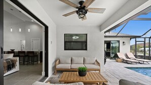 A modern outdoor living area with a wooden table, a sofa, and a ceiling fan. There is a pool visible in the background. - Paradise in front of the water (Cape Coral)