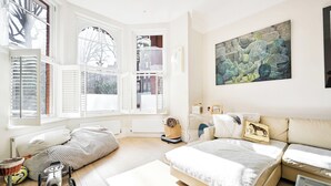 Un dormitorio moderno con una cama grande, una ventana con contraventanas, un cuadro en la pared y una pequeña mesa con una cesta.