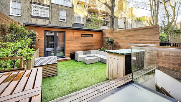Un patio moderno al aire libre con terraza de madera, un rincón de estar pequeño y un cerramiento de vidrio.