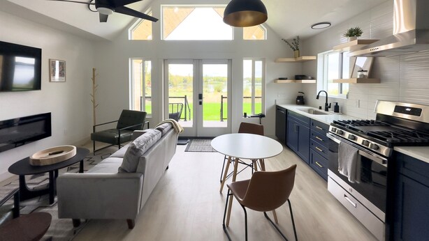 Ett modernt kök med en stor spis, en matplats med ett runt bord och stolar samt ett vardagsrum med en soffa och en tv.