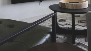 Ett modernt vardagsrum med en stor, platt-TV som är monterad på väggen, ett träbord och en grön, vadderad bänk.