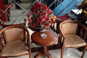 Zwei Holzstühle mit gepolsterten Sitzflächen und Rückenlehnen, ein kleiner runder Holztisch mit einer dekorativen Blumenvase und eine Glastrennwand im Hintergrund.